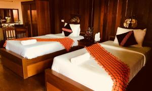 a bedroom with three beds with orange and white sheets at Mitkhoonyoum Hotel in Ban Khun Yuam