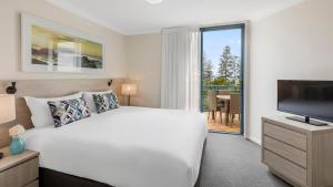 a bedroom with a large white bed and a television at Oaks Gold Coast Calypso Plaza Suites in Gold Coast