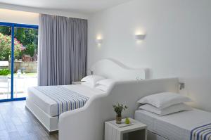 a white bedroom with two beds and a balcony at Lindia Thalassa in Pefki