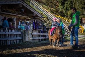 Um homem e uma criança a montar um pónei com uma criança. em Alpin Family Resort Seetal em Kaltenbach