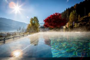 a pool of water with the sun in the background at Alpin Family Resort Seetal in Kaltenbach