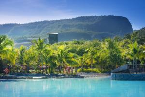une piscine avec des palmiers et une montagne en arrière-plan dans l'établissement Rio Quente Resorts - Eco Chalés, à Rio Quente