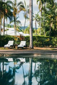 two white benches next to a pool with palm trees at Paradise Links Resort Port Douglas in Port Douglas