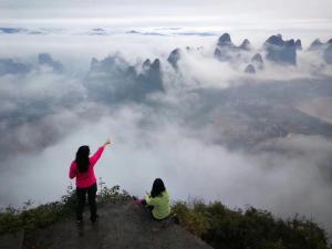 two women standing on top of a mountain with clouds at Yangshuo Yunshe Mountain Guesthouse in Yangshuo