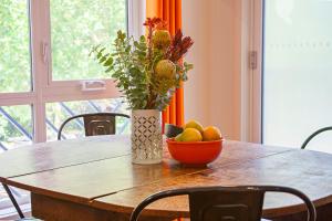 una mesa con un jarrón de flores y un tazón de fruta en One of a Kind Apartments, en Canberra