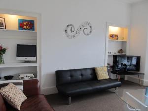a living room with a black leather couch and a television at The Beatnik, Victorian townhouse apartment with parking in Plymouth