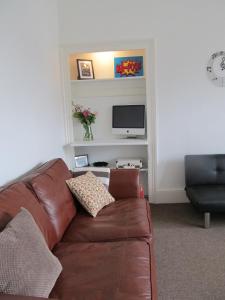 a living room with a brown leather couch and a tv at The Beatnik, Victorian townhouse apartment with parking in Plymouth