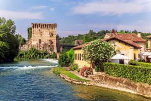 a river with houses and a castle and a tower at GardaBeds Adults Only in Castelnuovo del Garda