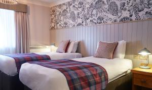 two beds in a hotel room with a plaid blanket at The Bear Hotel by Greene King Inns in Hungerford