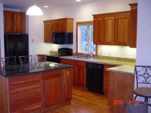 una cocina con armarios de madera y electrodomésticos negros en Breathtaking New Premier Lake Champlain Waterfront Escape!, en Addison