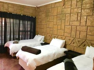 Habitación con 3 camas y pared de piedra. en Klein Paradys Lodge - Polokwane en Polokwane