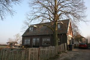 a house with a tree in front of a fence at Unique place on the river Waal in Heerewaarden