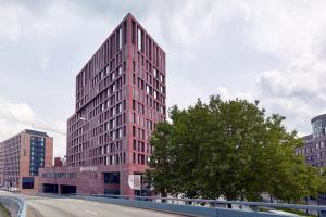 um alto edifício vermelho com uma árvore em frente a uma rua em HYPERION Hotel Hamburg em Hamburgo