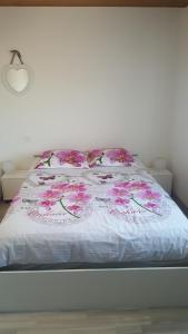 a bed with a white comforter with pink flowers on it at La Maison des Oiseaux in Eu