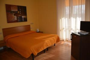 a bedroom with a bed with an orange bedspread and a television at Piccolo Hotel in Rosignano Solvay