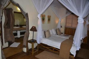 a bedroom with a bed with curtains and a bathroom at Moholoholo Forest Camp in Hoedspruit
