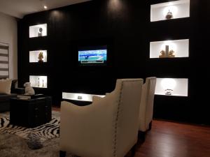 a living room with white chairs and a tv on a black wall at Nicotel Apartments in Abuja