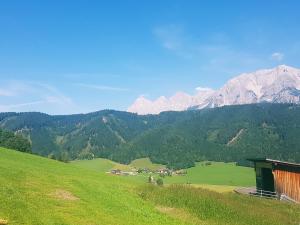 ein grüner Hügel mit einem Haus und Bergen im Hintergrund in der Unterkunft Götschlhof in Schladming