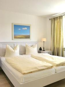 un letto bianco con lenzuola e cuscini bianchi di Ferienwohnung *SonnenOase* a Wittdün