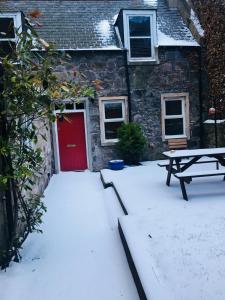 une maison avec une porte rouge et une table de pique-nique dans la neige dans l'établissement The Cottage, à Aberdeen