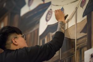 a man with glasses painting a flag on a wall at King Wow Inn in Tainan