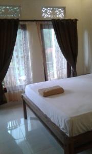 a bed in a room with two windows at Madu Sentana House in Ubud