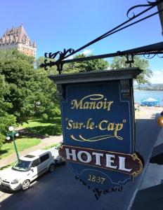 Manoir Sur le Cap في مدينة كيبك: لافته لفندق فيه سياره متوقفه في موقف سيارات