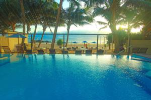 a swimming pool with chairs and palm trees and the ocean at Beacon Beach Hotel Negombo in Negombo