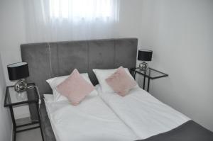a bed with white sheets and pink pillows and two lamps at Apartament Wilenska in Mrągowo