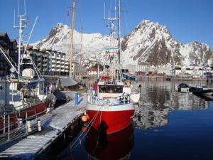 un bateau rouge et blanc amarré sur un quai avec des montagnes dans l'établissement Svolvær Havn Apartments, à Svolvær