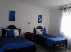 a bedroom with two beds with blue sheets and a window at Hotel Branco II in Praia da Vitória