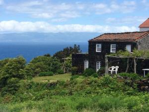 an old house with a white chair in front of it at Casa Da Lava in São Roque do Pico