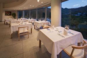 um restaurante com mesas e cadeiras brancas e janelas em Takamiya Hotel Rurikura Resort em Zao Onsen