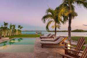 uma piscina com espreguiçadeiras e palmeiras e o oceano em Hotel CasaBakal - A pie de Laguna - Bacalar em Bacalar