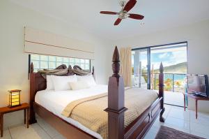 a bedroom with a bed with a ceiling fan and a television at at Waterfront Whitsunday Retreat - Adults Only in Airlie Beach