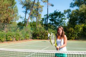 una joven sosteniendo una raqueta de tenis en una pista de tenis en Résidence Goélia La Marina de Talaris, en Lacanau
