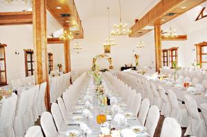 Długa sala bankietowa z białymi stołami i krzesłami w obiekcie Hotel Chutor Kozacki w mieście Łukowe