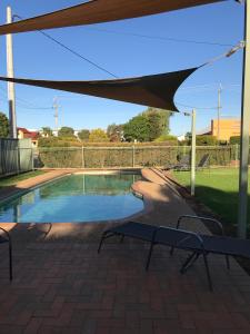 a swimming pool with a umbrella and a bench at The Kidman Wayside Inn in Griffith
