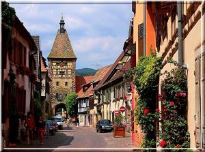 eine Stadtstraße mit Gebäuden und einem Uhrturm in der Unterkunft S'Harzala Rouge in Bergheim