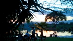 a group of people sitting around a table by a lake at Voyager Ziwani Tented Camp in Ziwani