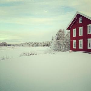 uma casa vermelha na neve ao lado de um campo em Norrsjön em Sörsjön