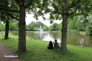 Due persone sedute sull'erba di fronte a uno stagno di Romantic ground floor suite in Pijp near Sarphatipark ad Amsterdam