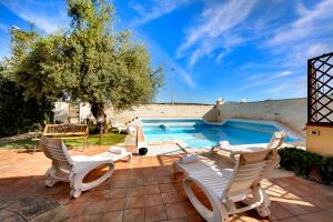 eine Terrasse mit weißen Stühlen und einem Pool in der Unterkunft Villa dell'Ulivo in Marina di Ragusa