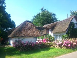 a white cottage with a thatched roof and flowers at Föhrer Friesenkate Ost in Nieblum