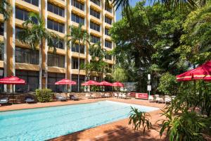 a swimming pool in front of a hotel with red umbrellas at Frontier Hotel Darwin in Darwin
