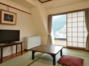 a living room with a tv and a table and a window at Riverside Uedakan in Chikuma