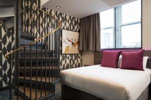 a bedroom with a bed with purple pillows and a staircase at Roomzzz Manchester Victoria in Manchester