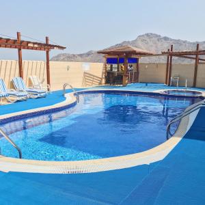 a large blue swimming pool with chairs and a building at Mirage Hotel Al Aqah in Al Aqah