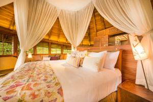 a bedroom with a large white bed with curtains at Origins Lodge in Bijagua