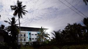 a building with palm trees and a cloudy sky at Indeevaram Residency in Trivandrum